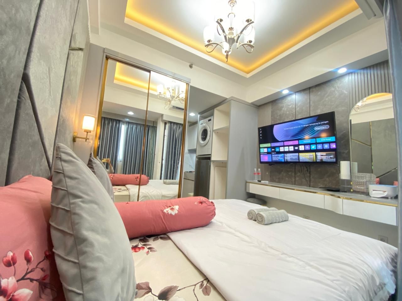 A hotel room with a bed, a TV, a mirror, and a bathroom visible through an open door.