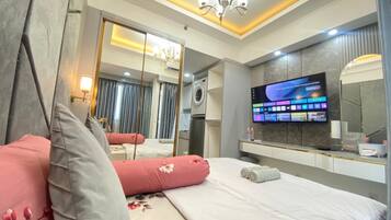 A hotel room with a bed, a TV, a mirror, and a bathroom visible through an open door.