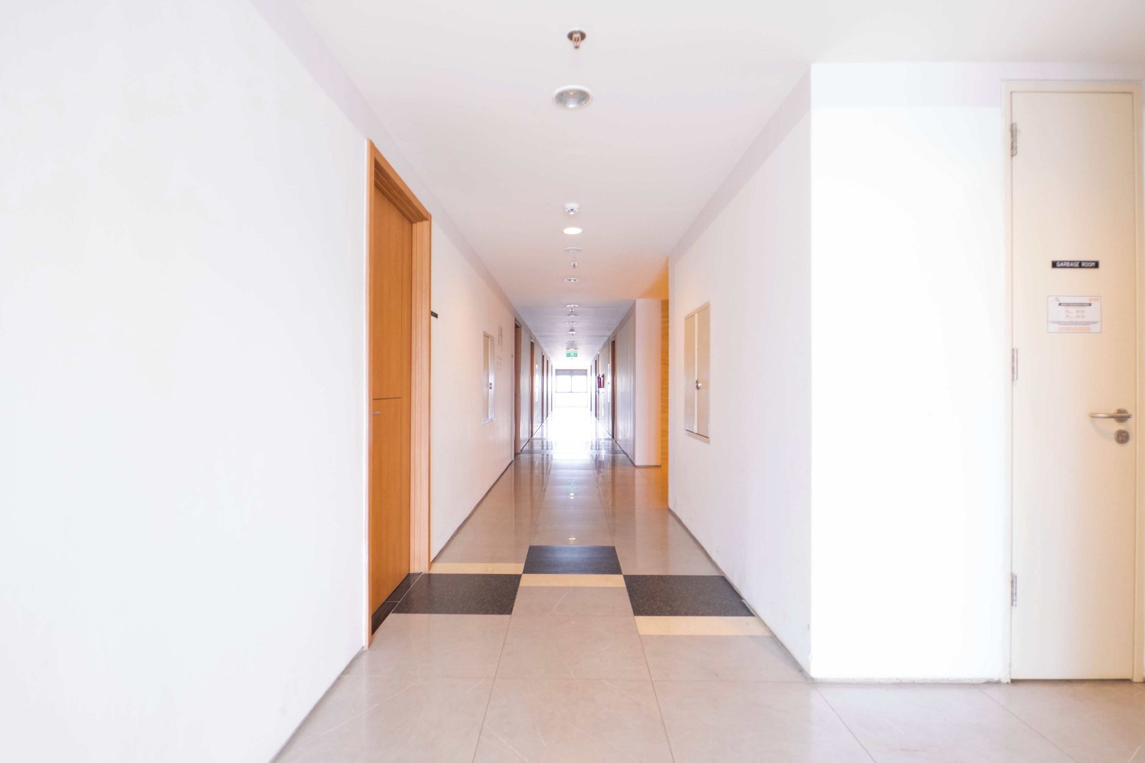 Un pasillo largo y estrecho con piso a cuadros que conduce a una puerta con un letrero que indica depósito de basura.