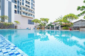 Una piscina con bordo piastrellato, circondata da alberi e un edificio a più piani con balconi.