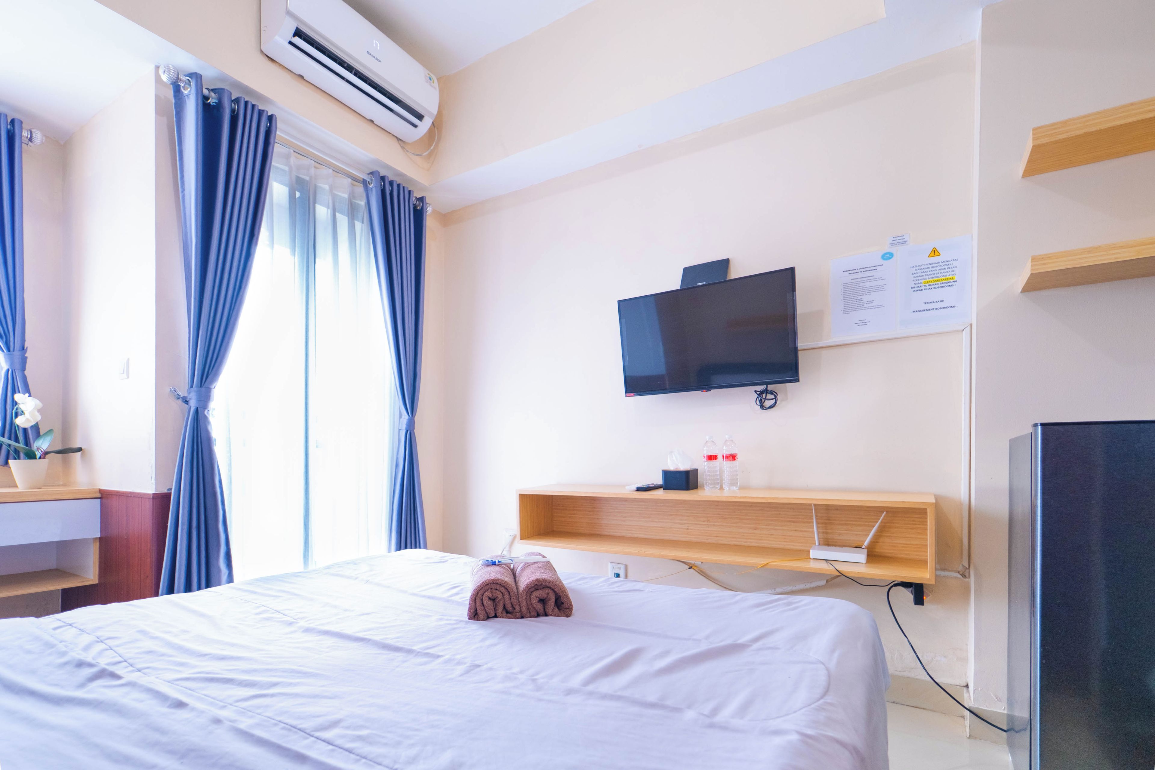 Camera d'albergo con un letto, una televisione a muro, una scrivania con un computer e una finestra con tende.