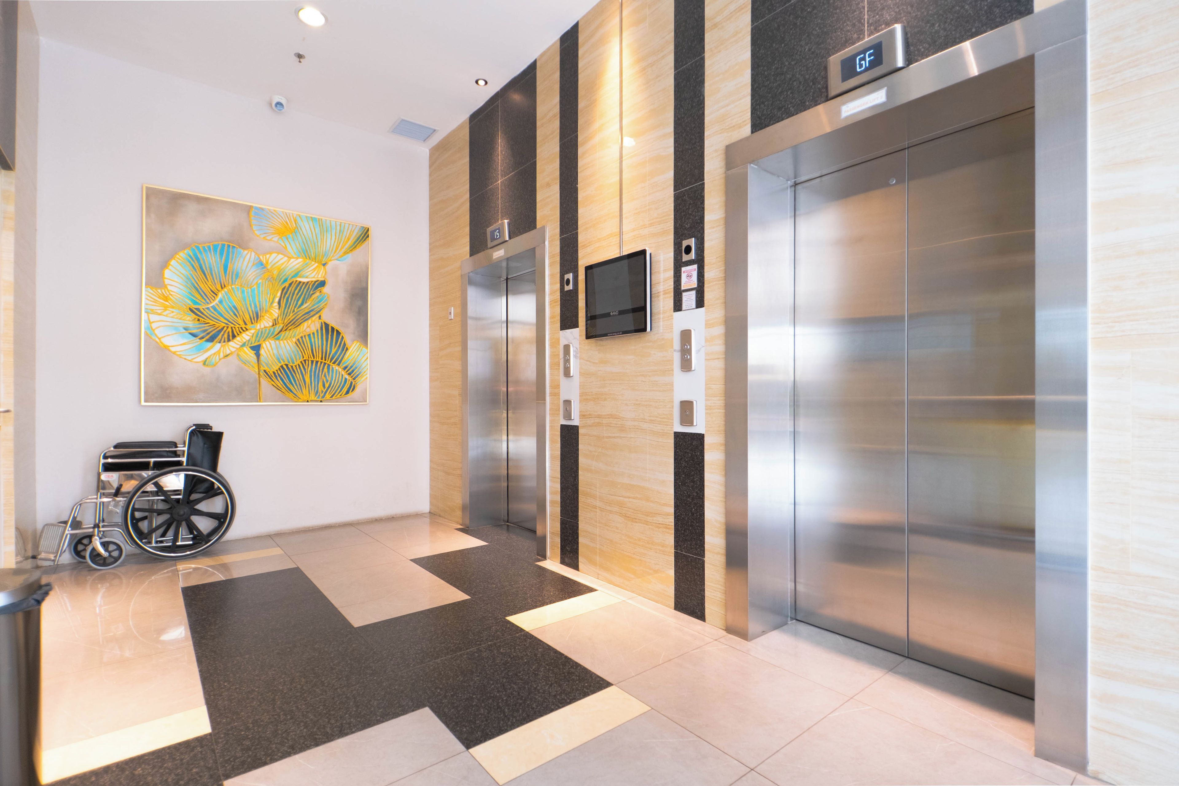 An elevator area with a wheelchair, a digital display, and a large abstract painting on the wall.
