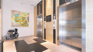 An elevator area with a wheelchair, a digital display, and a large abstract painting on the wall.