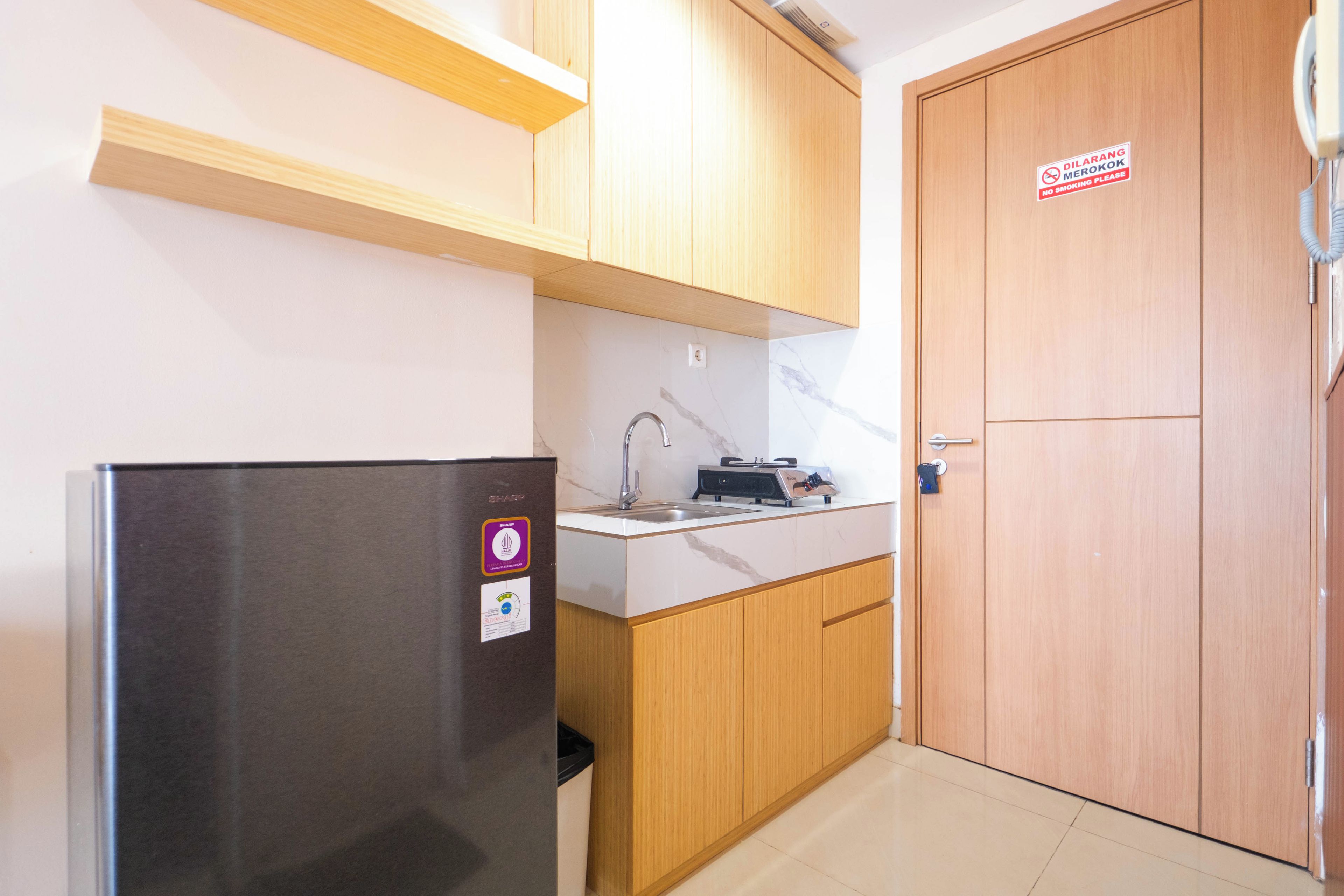 A compact kitchen with a stainless steel refrigerator, wooden cabinets, a marble countertop, and a door with a no smoking sign.