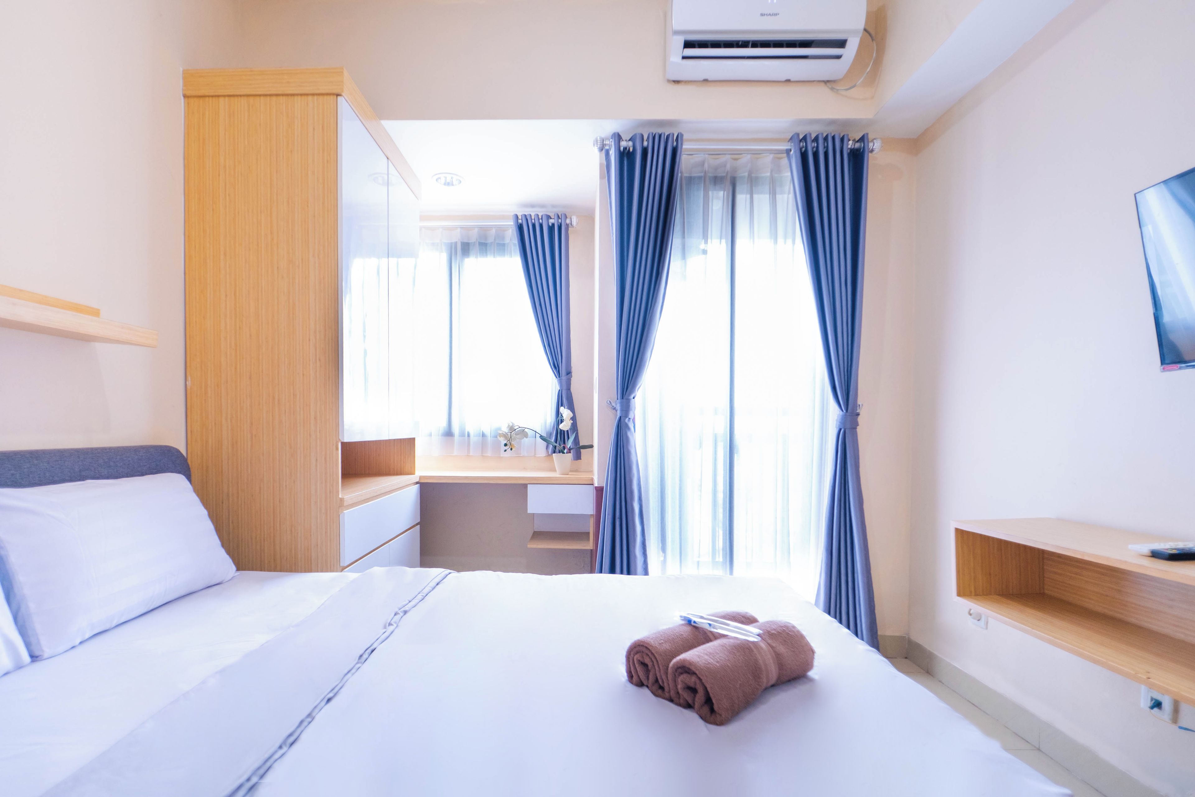 A hotel room with a bed, a desk, a mirror, and a TV.