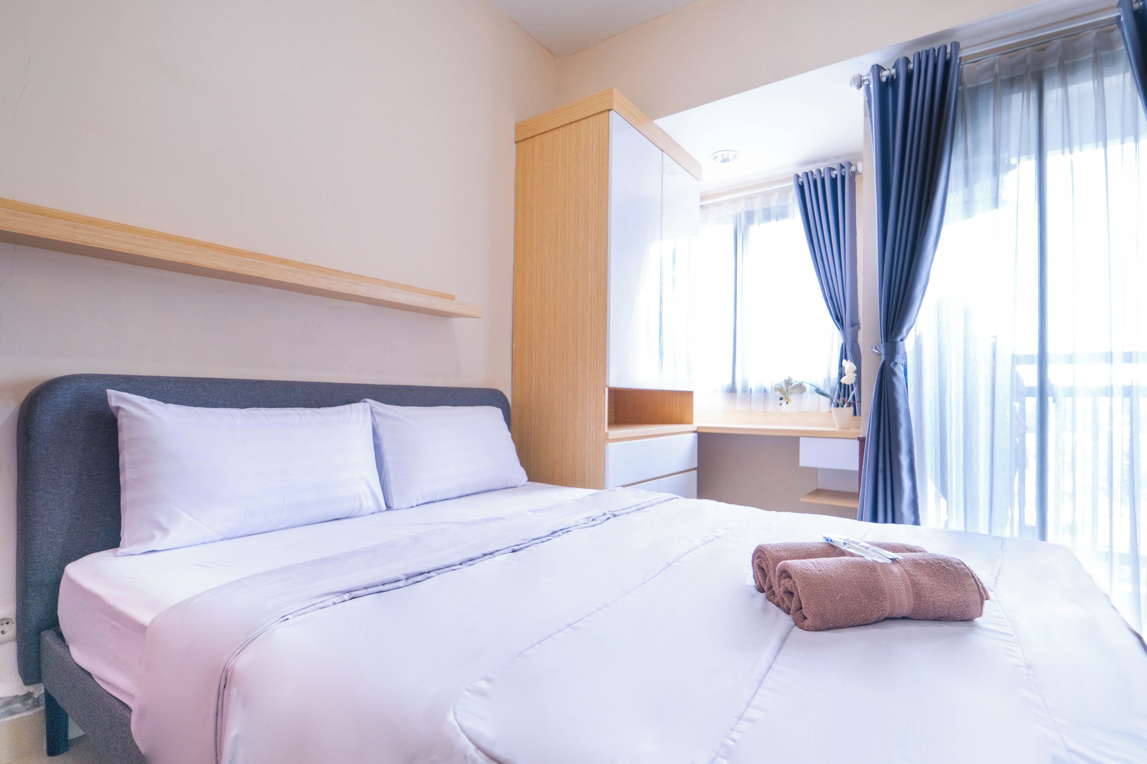 A hotel room with a bed, a bedside table, a mirror, and a window with curtains.