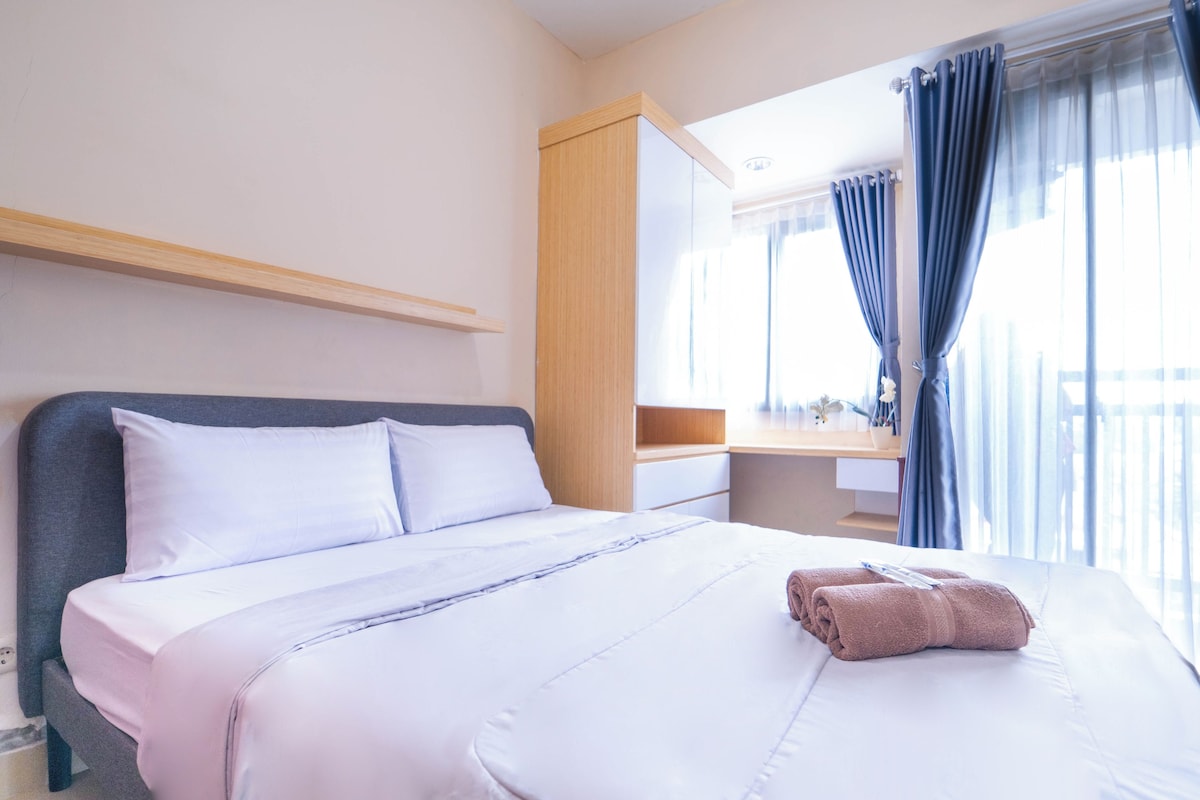 A hotel room with a bed, a bedside table, a mirror, and a window with curtains.