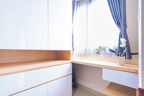 A room with a built-in desk, a window with curtains, and a potted plant on the windowsill.