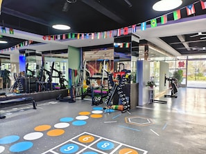Un gimnasio con diferentes equipos de ejercicio, un espejo grande en la pared y un suelo con baldosas numeradas.