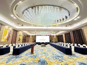 A conference room with a large screen, rows of tables, and a decorative ceiling.