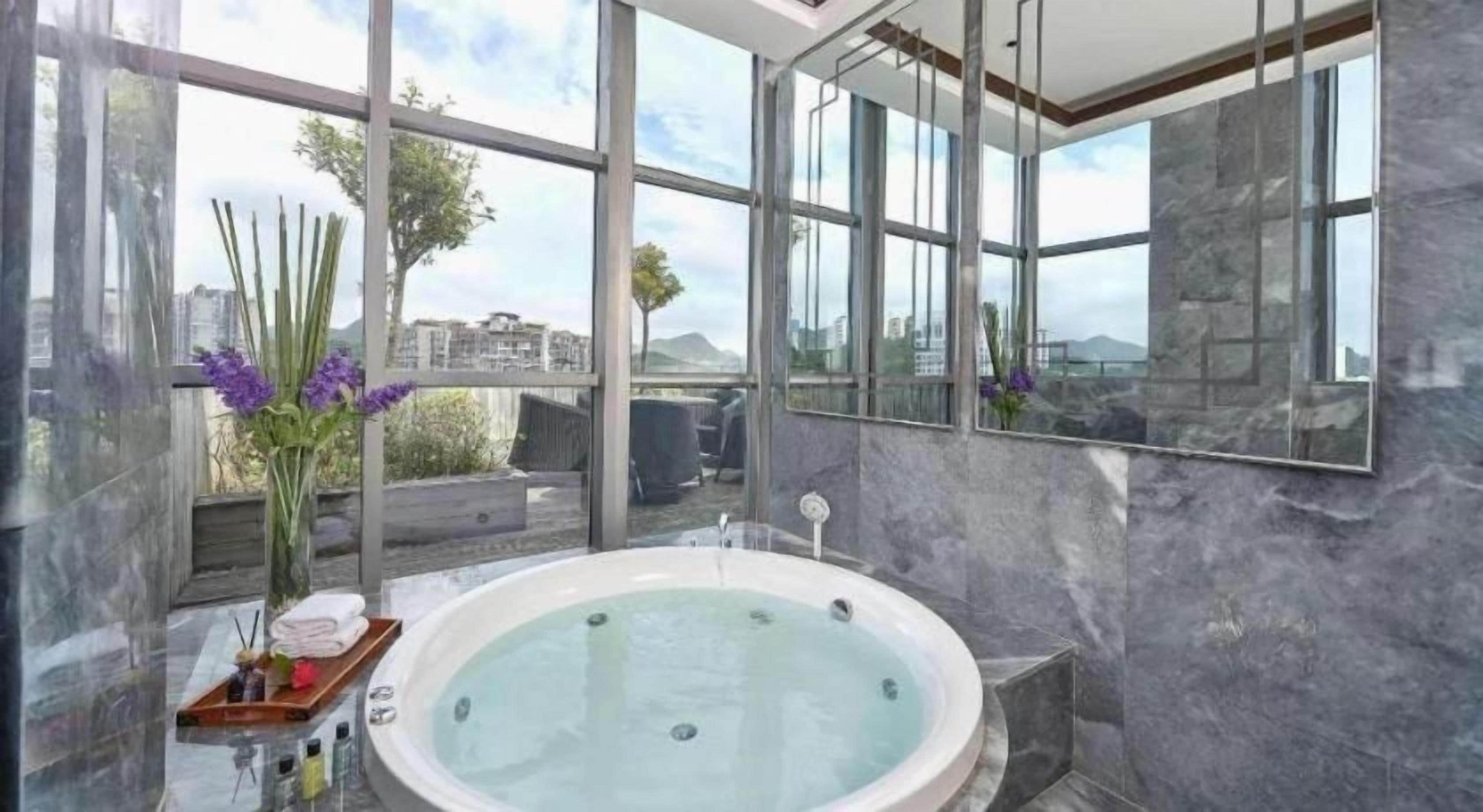 A modern bathroom with a large bathtub, a wooden tray with towels, and a vase of flowers.