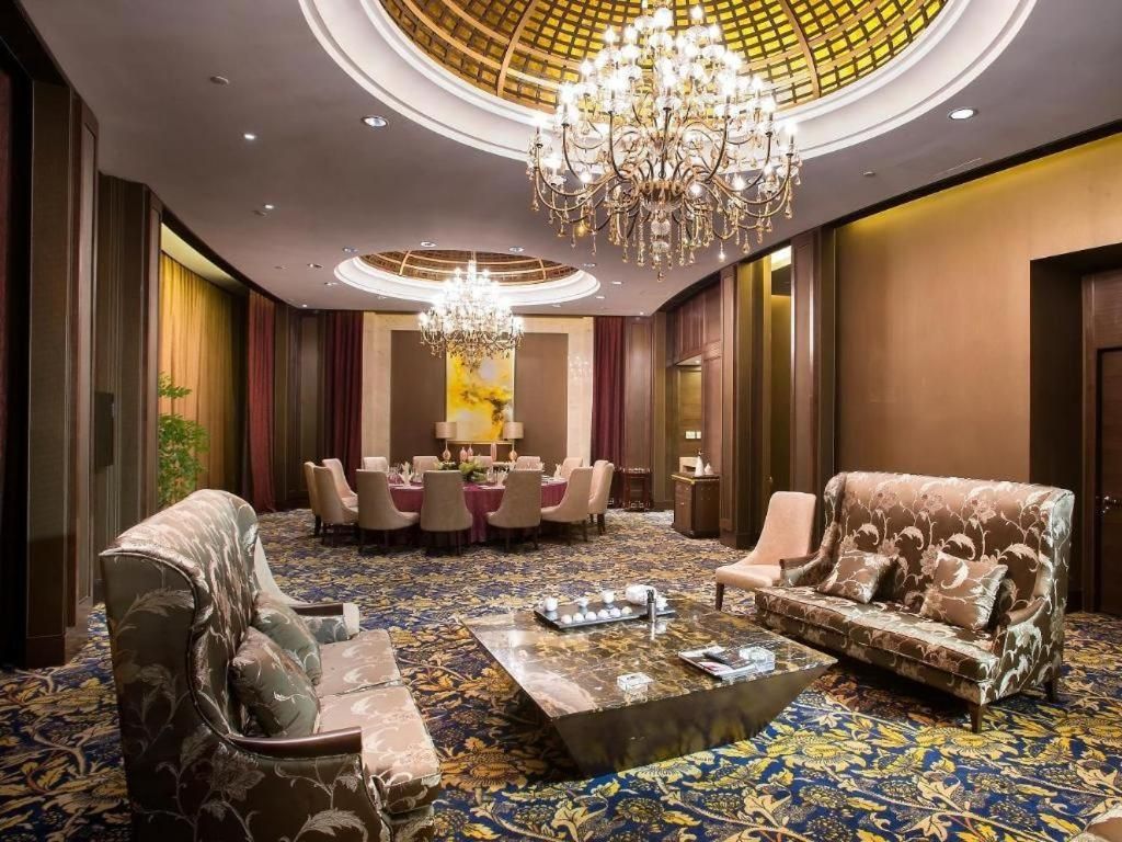 A luxurious hotel lobby with a grand chandelier, plush seating, and a patterned carpet.