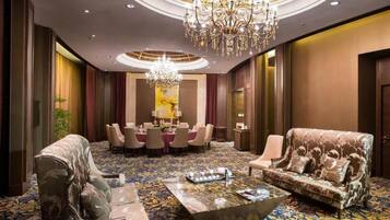 A luxurious hotel lobby with a grand chandelier, plush seating, and a patterned carpet.