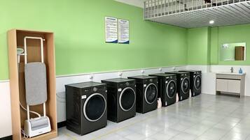 A laundry area with multiple washing machines, a drying rack, and a sink.