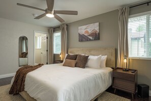 A bedroom with a bed, a ceiling fan, a bedside table with a lamp, and a painting on the wall. - Reunion House,  5 King Beds, Hot Tub + Sauna , Mini Golf + Game Room (Arvada)