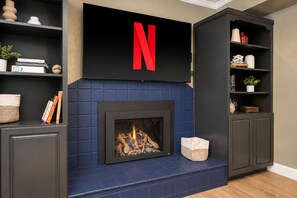 A modern living room with a fireplace, a television mounted above it, and built-in shelving with various items.