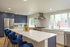 A modern kitchen with a central island, dark cabinets, stainless steel appliances, and a large window.