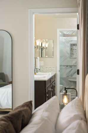 A hotel room with a bed, a bathroom with a mirror, a sink, and a light fixture.
