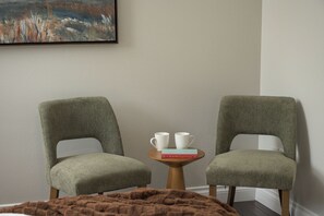 Una habitación con dos sillones tapizados, una pequeña mesa de madera con dos tazas blancas y un libro, y un cuadro en la pared.