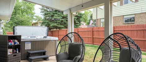 Un espace extérieur abrité, doté d'un ventilateur de plafond, d'un barbecue, de deux fauteuils en osier noirs et d'un espace de rangement sur lequel est apposée une pancarte indiquant « AVIS ».