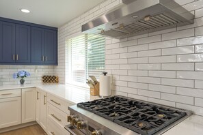 A modern kitchen with white subway tiles, a stainless steel range hood, and a gas stove. - Reunion House,  5 King Beds, Hot Tub + Sauna , Mini Golf + Game Room (Arvada)