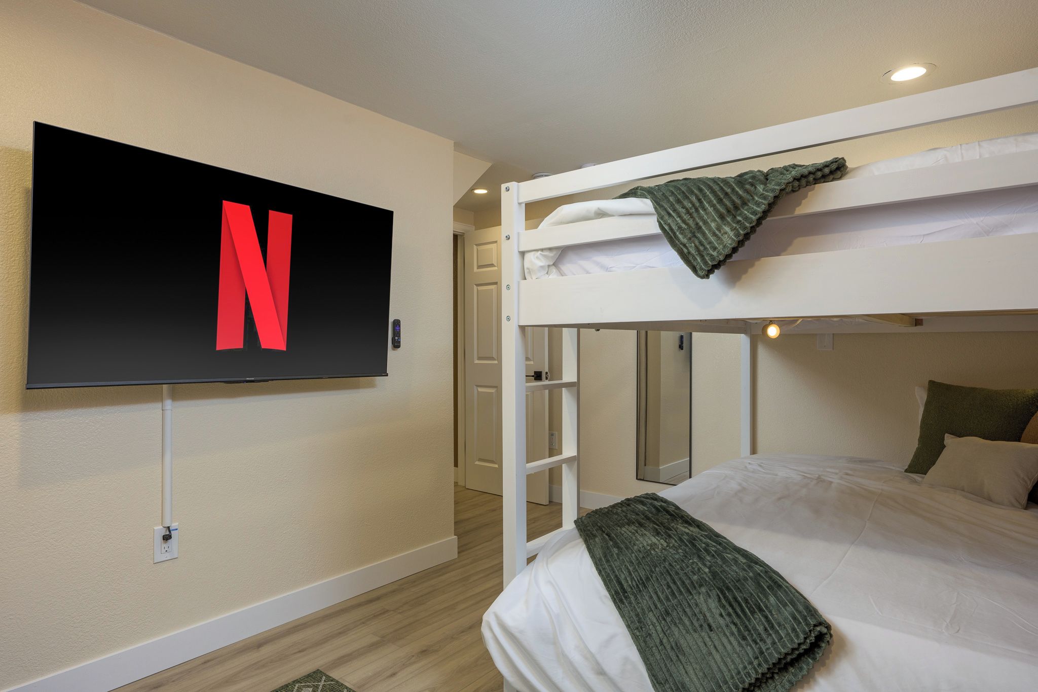 A room with a bunk bed, a television mounted on the wall, and a door leading to another room.