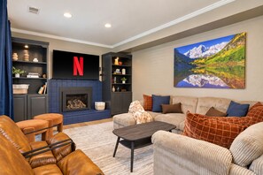 A modern living room with a fireplace, a Netflix logo, and a large mountain landscape painting.