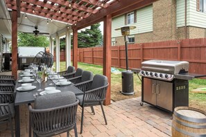 An outdoor patio with a long dining table set for a meal, a grill, and a pergola with string lights. - Reunion House,  5 King Beds, Hot Tub + Sauna , Mini Golf + Game Room (Arvada)