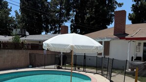 A swimming pool with a white umbrella, surrounded by a wooden deck and a brick building. - The Northridge Nook: A Cozy 1-bedroom house in Los Angeles with AC & Pool Access (Los Angeles)