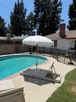 Ein Swimmingpool mit einem weißen Sonnenschirm, umgeben von einer Holzterrasse und einem Backsteinhaus.