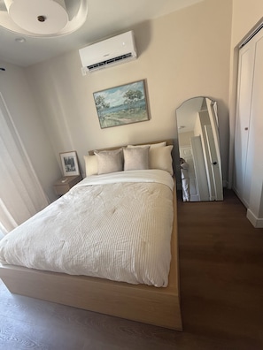 Ein Schlafzimmer mit einem Bett, einem Nachttisch, einer Wand-Klimaanlage, einem Bild und einem Spiegel.