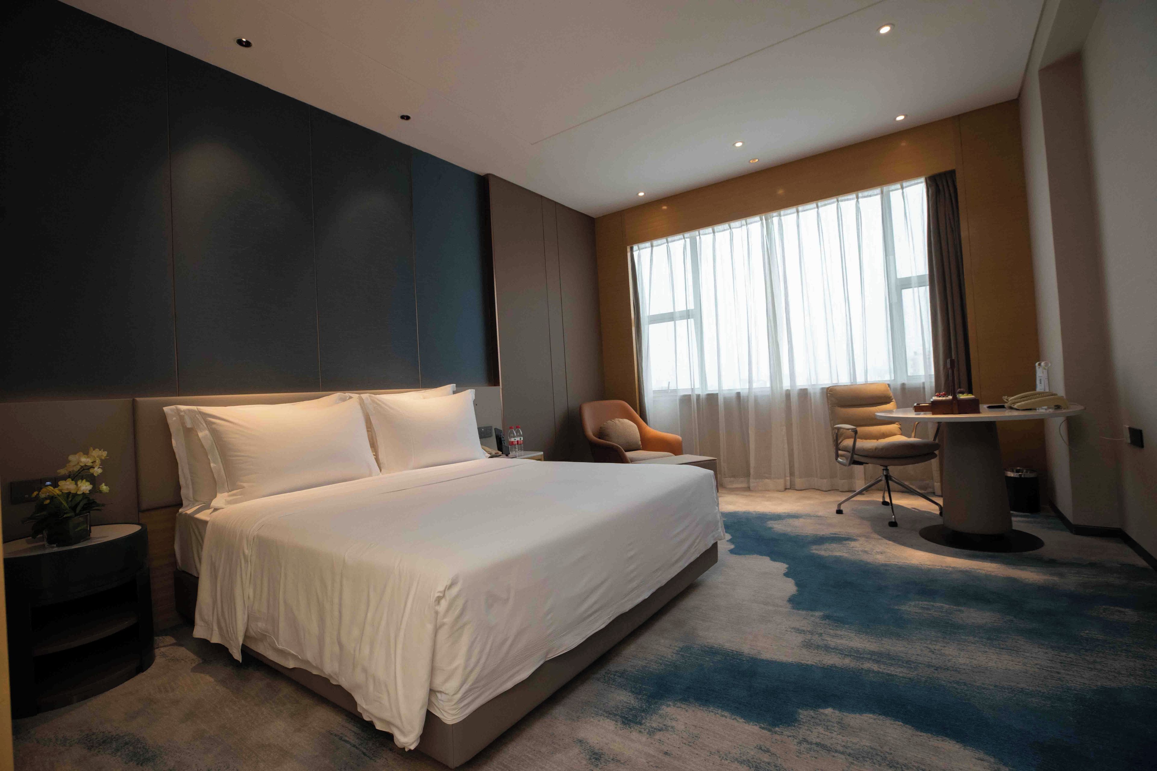 A modern hotel room with a large bed, a desk, and a chair.