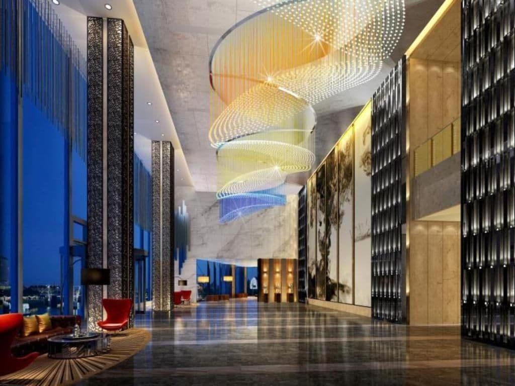 A spacious lobby with a modern design, featuring a curved ceiling light fixture and a seating area with red chairs.