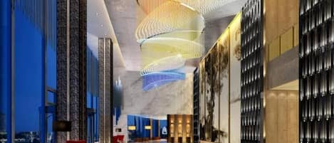 A spacious lobby with a modern design, featuring a curved ceiling light fixture and a seating area with red chairs.