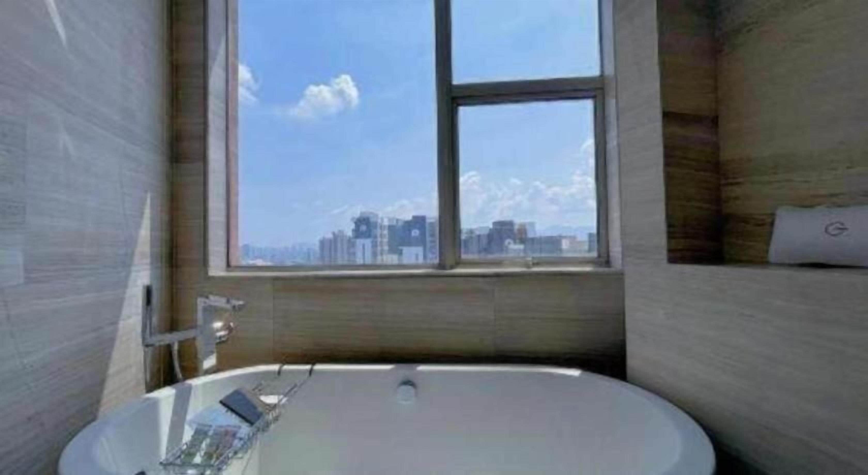 A modern bathroom with a large bathtub, a window with a city view, and a built-in shelf.