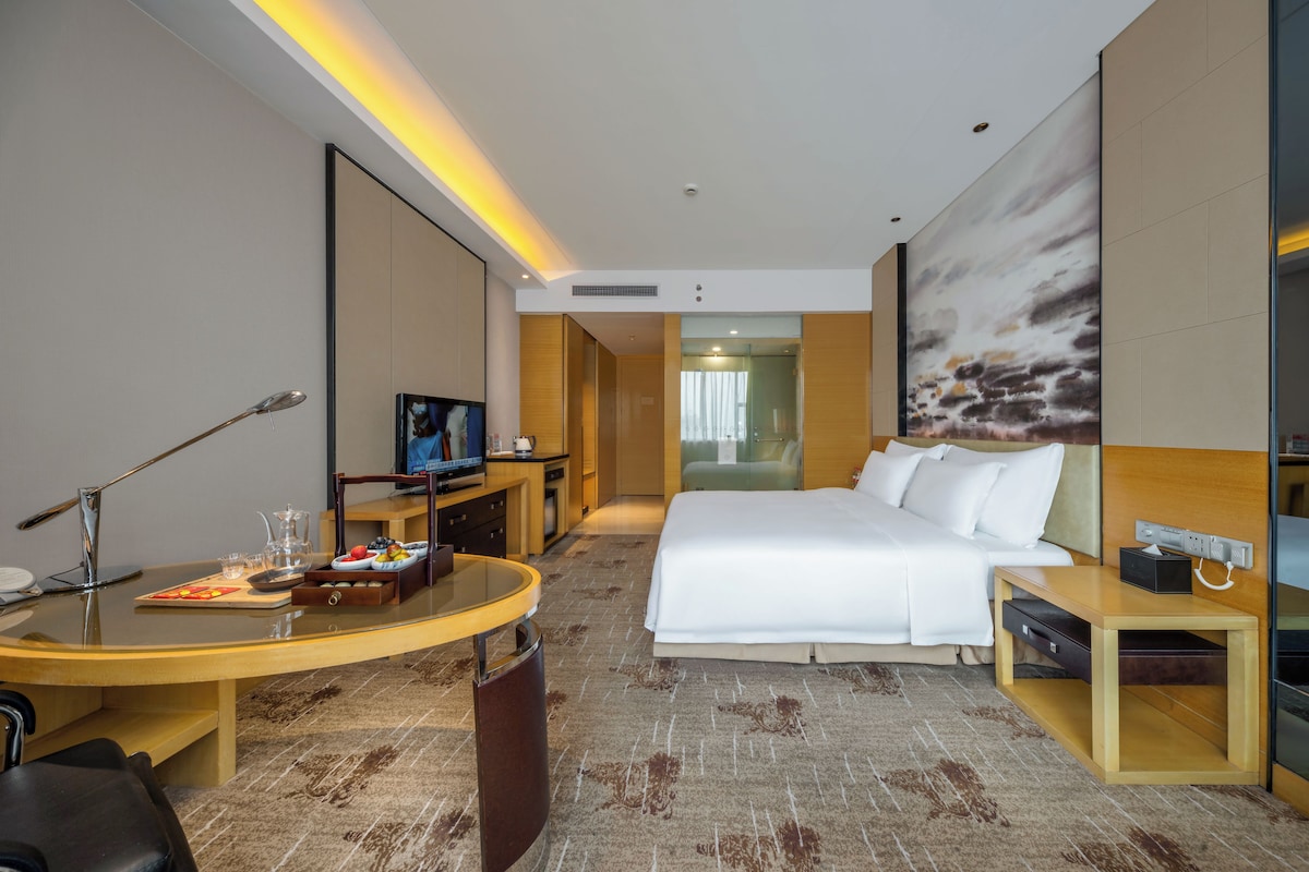 Una habitación de hotel con cama, escritorio con computadora, televisor y ventana grande.