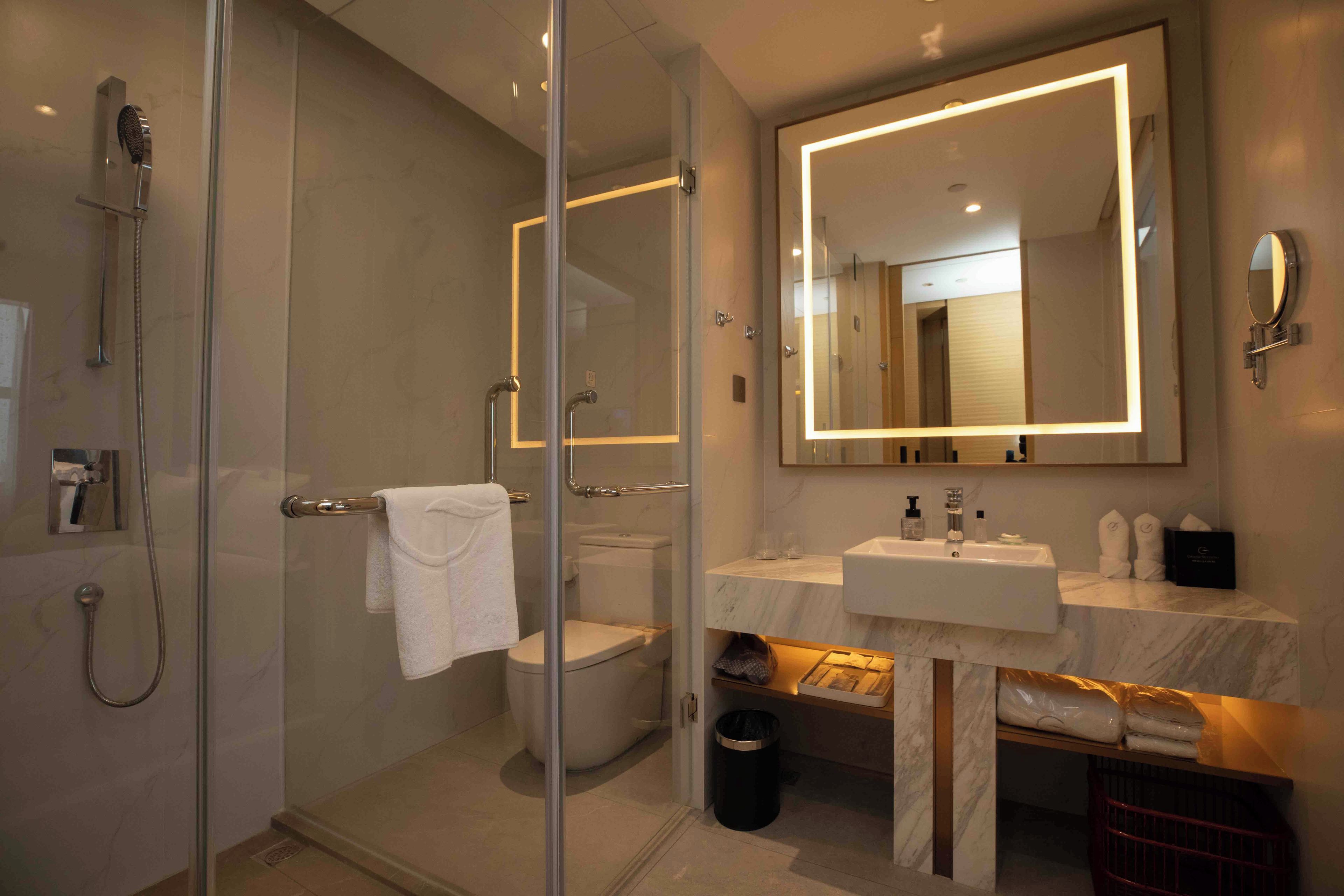 Un baño moderno con ducha envuelta en vidrio, inodoro, lavabo con encimera de mármol y un espejo grande.