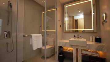 Un baño moderno con ducha envuelta en vidrio, inodoro, lavabo con encimera de mármol y un espejo grande.