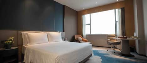 Une chambre d’hôtel moderne avec un grand lit, un bureau, une chaise et une fenêtre avec des rideaux.