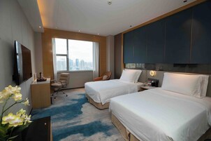 Habitación de hotel con dos camas, un escritorio, una silla, un televisor y un ventanal con vista a la ciudad.