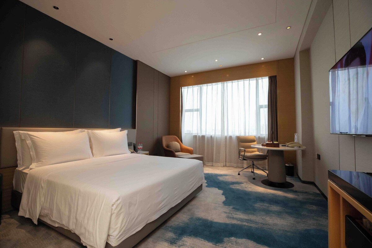 Una habitación de hotel con una cama grande, un escritorio, una silla y un televisor.