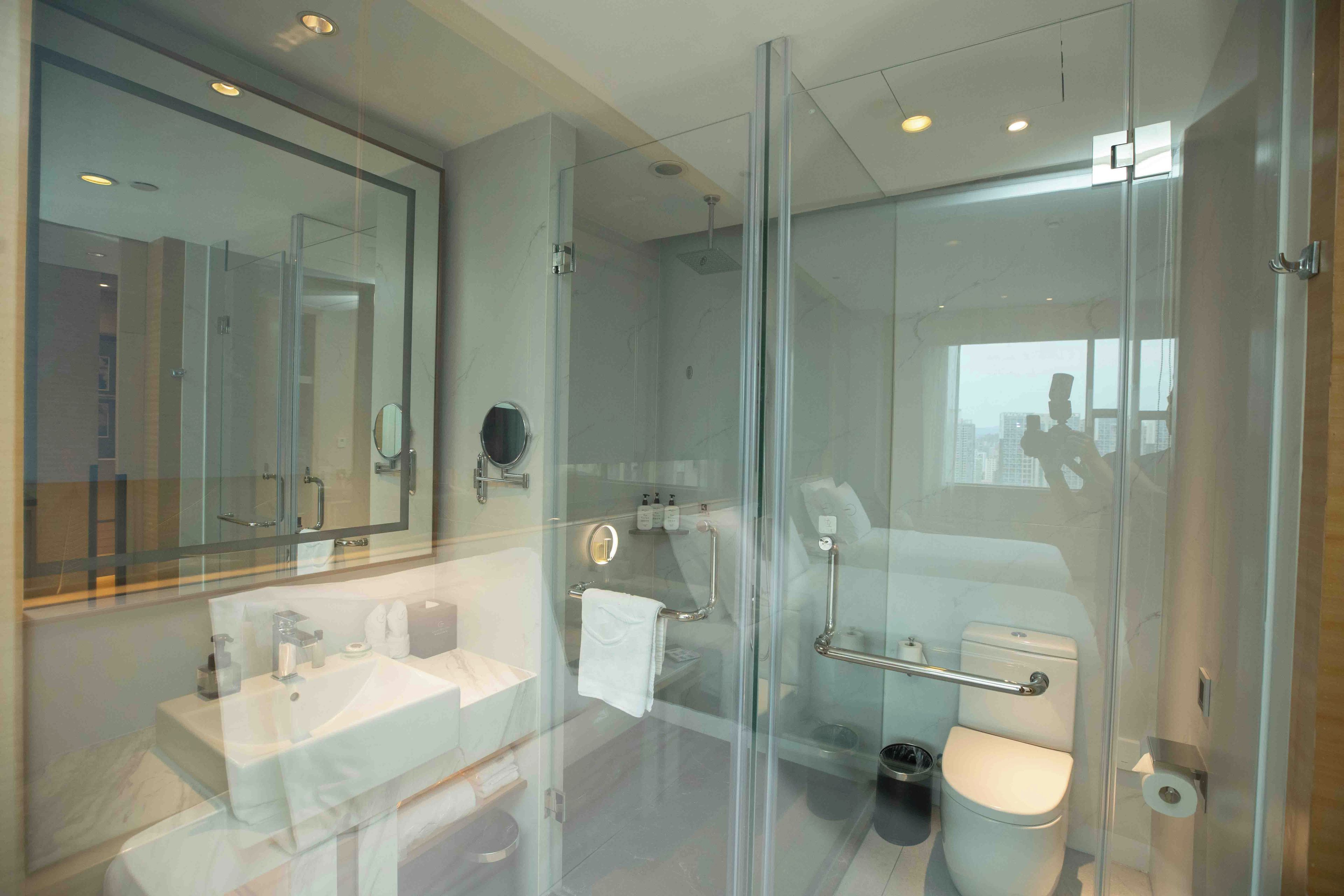 Ein modernes Badezimmer mit Duschkabine aus Glas, einem großen Spiegel und einer Toilette mit Handlauf.