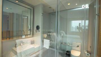 Ein modernes Badezimmer mit Duschkabine aus Glas, einem großen Spiegel und einer Toilette mit Handlauf.