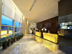Un vestíbulo de hotel con una recepción, plantas en macetas y un amplio ventanal.