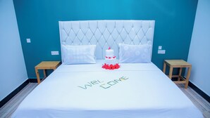 Cama bem arrumada com colcha branca, duas almofadas e um arranjo decorativo de flores vermelhas.