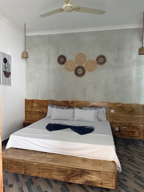 A room with a bed, a ceiling fan, a wall-mounted light fixture, and a decorative wall piece.