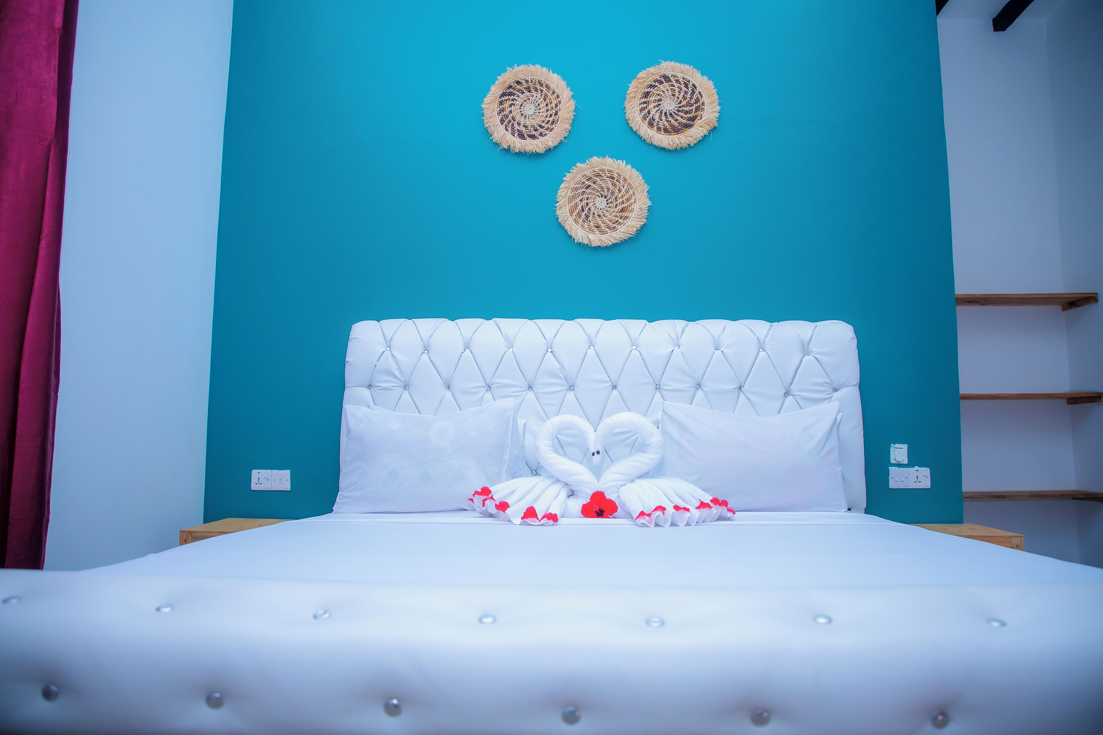 A bed with a tufted headboard, white pillows, and a decorative swan made of towels.