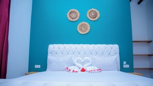 Uma cama com cabeceira estofada, almofadas brancas e um cisne decorativo feito de toalhas.
