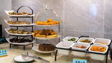 A buffet with multiple dishes, including a variety of Asian cuisine, arranged on tiered stands and in serving dishes.