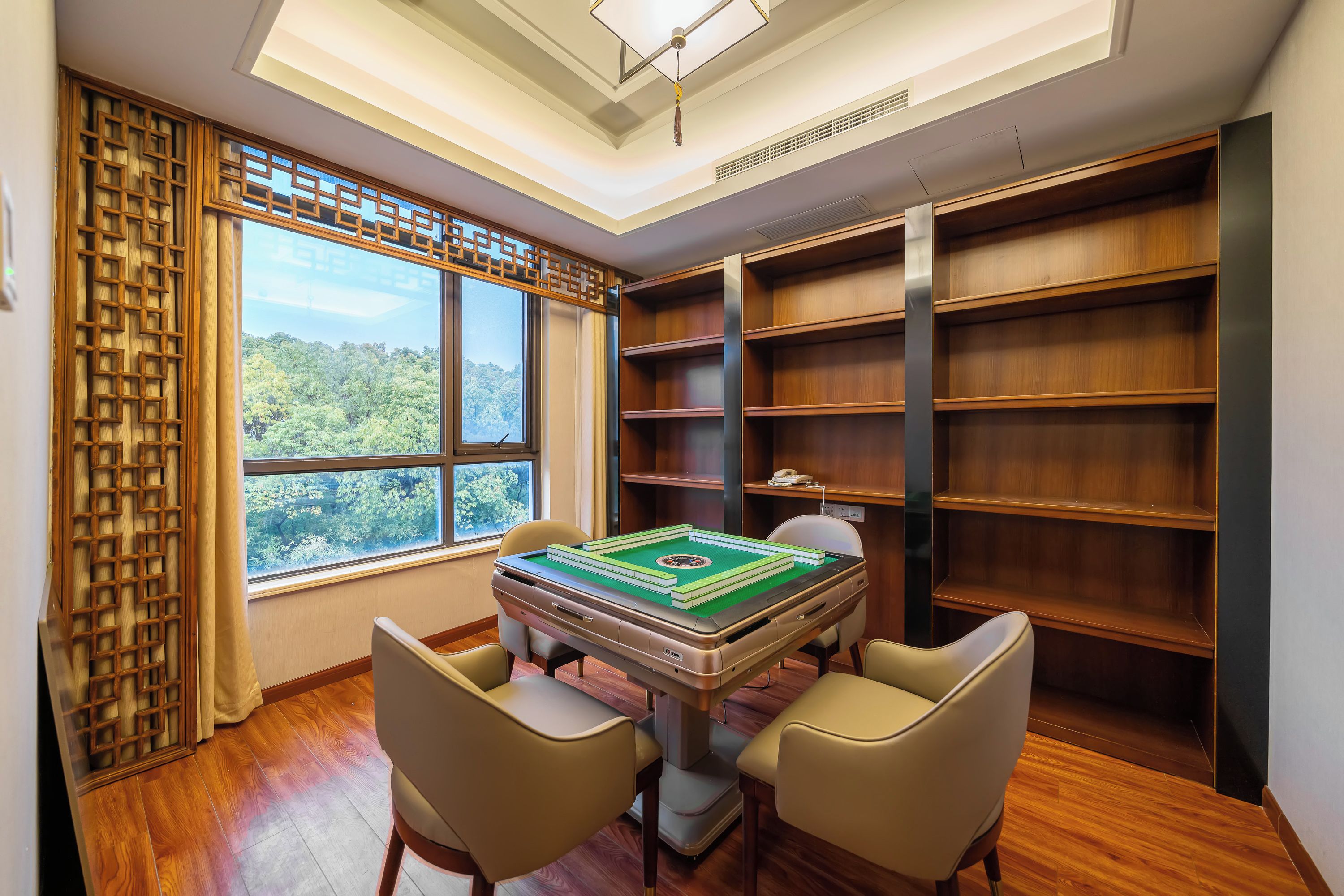 Une pièce avec une table basse recouverte d’un tatami, deux chaises, une bibliothèque et une fenêtre donnant sur des arbres.